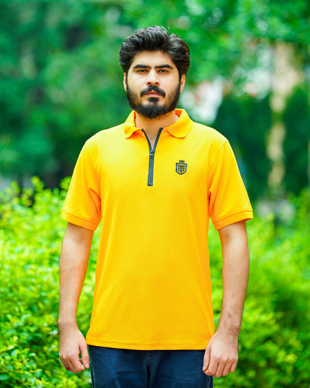 Man wearing a yellow polo shirt with a logo in a green outdoor setting